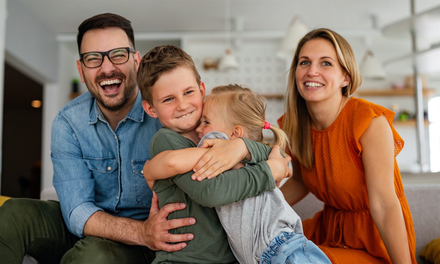 A warm family at home - two parents and two young children laughing and hugging together.